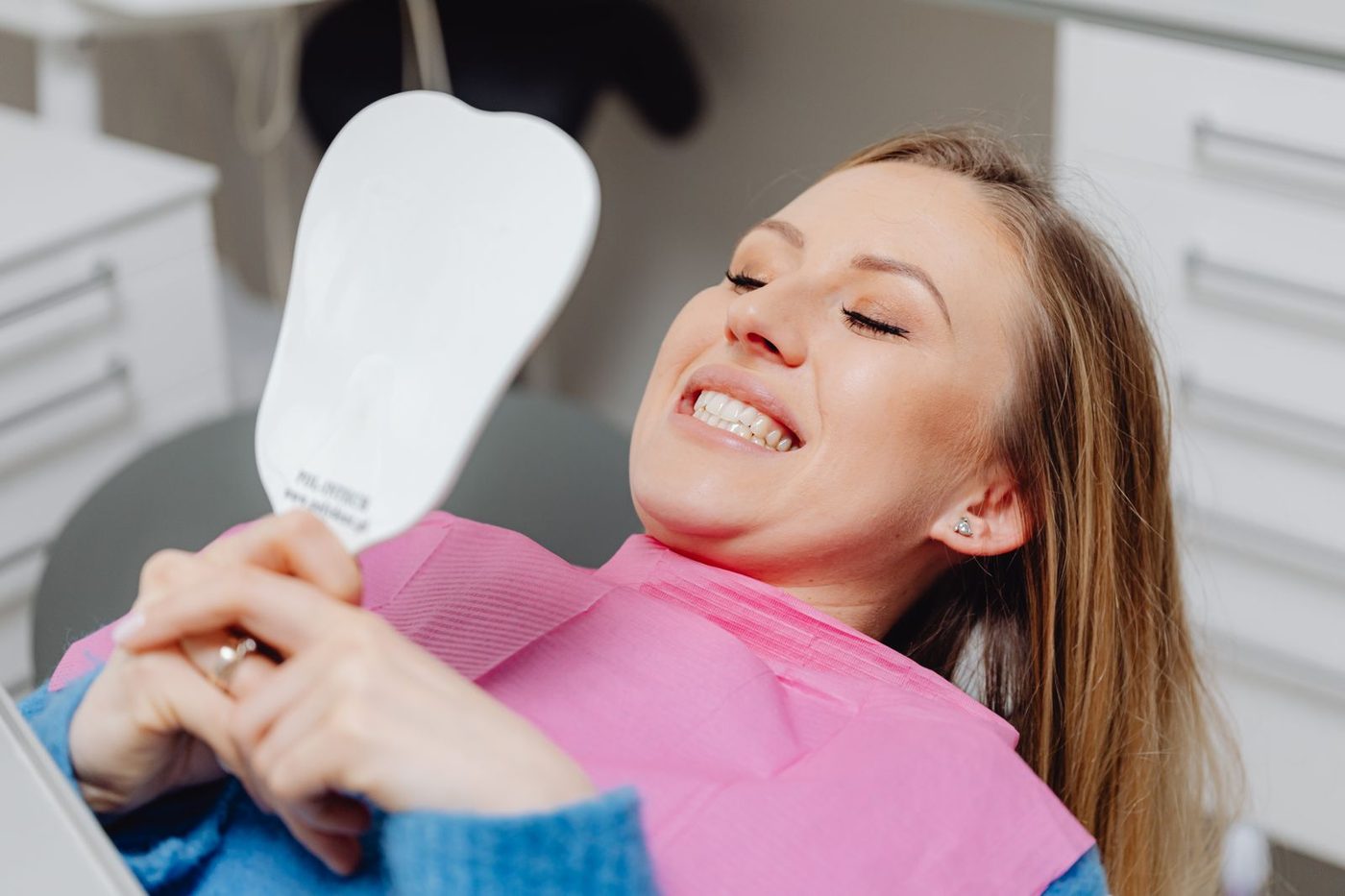 Paciente sorrindo, olhando o próprio sorriso no espelho após atendimento